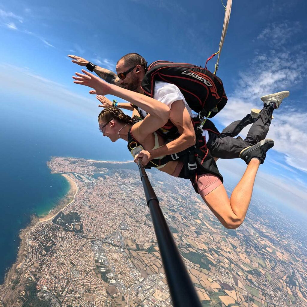 Lola en saut tandem à 4 000 mètres, bras tendus, au-dessus des Sables-d'Olonne moniteur Théo en harnais Legend, côte atlantique et plages vendéennes visibles en arrière-plan